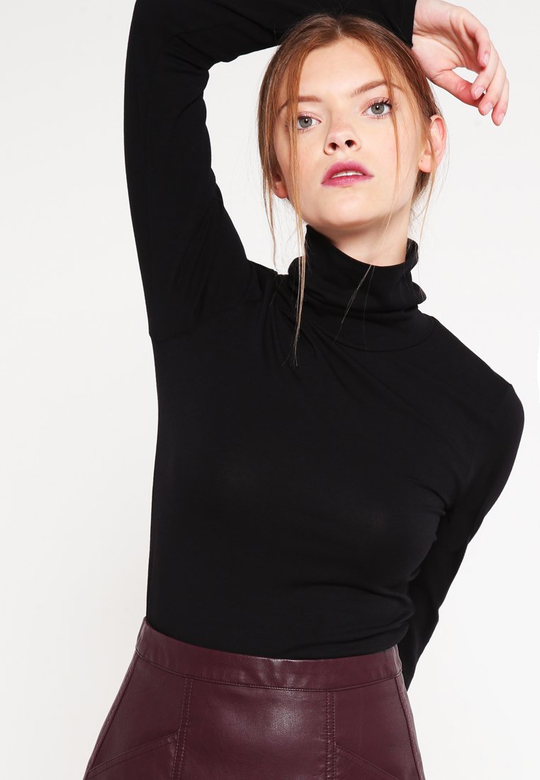 Svart høyhalset topp laget av elastisk stoff med lange ermer. Kombinert med et bordeaux skinnskjørt med geometriske sømmer.