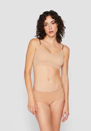 Seamless, nude bralette with thin adjustable straps and a v-neckline, paired with matching low-rise underwear, both made from smooth fabric.