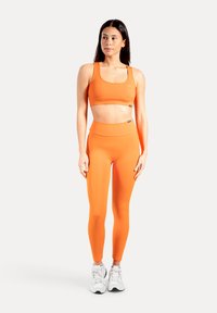 Heldere oranje sportbeha en legging van rekbaar materiaal, met een strak ontwerp en een hoge taille. Witte sneakers maken de outfit compleet.