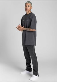 Tmavě šedé oversized tričko s krátkým rukávem, na přední straně s minimalistickým textem. V kombinaci s černými džíny a bílými teniskami.