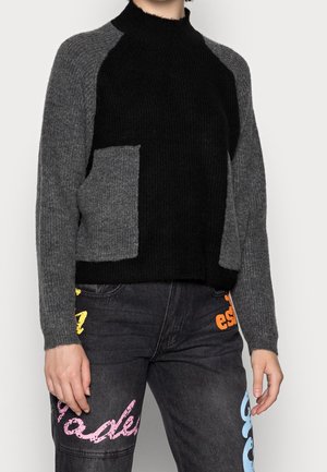 Sort og grå strikket sweater med et tekstureret, ribbet design. Har en mock neck og en lomme foran på venstre side.