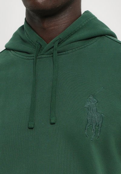 Grön hoodie med en känguruficka, justerbara snören och en präglad hästridarlogo på framsidan. Mjuk tygkvalitet, avslappnad passform.