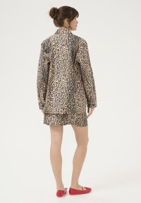 Abito camicia con stampa leopardata in tonalità sabbia e nero, caratterizzato da maniche lunghe e una vestibilità comoda, abbinato a scarpe flat rosse.