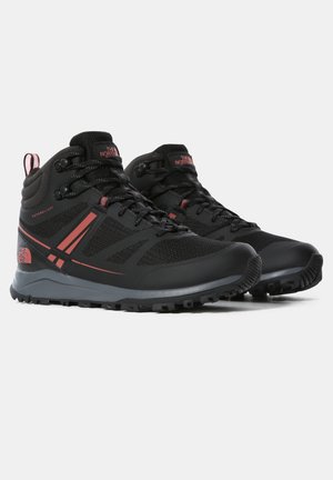 Czarne i różowe buty do wędrówek North Face o średniej wysokości, z teksturowanymi podeszwami i zapięciami na sznurowadła, ustawione pod kątem w prawo na białym tle.