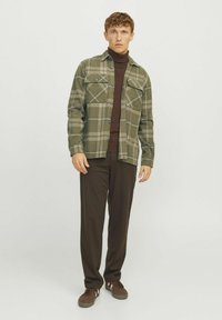 Groen en grijs geruit overhemd met twee borstzakken, gedragen over een bruine coltrui, gecombineerd met donkerbruine broek en bruine schoenen.