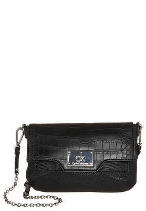 Black Calvin Klein crossbody bag with textured flap, silver logo plate, and chain strap on white background.