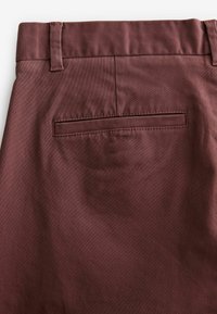 Pantalons en tissu bordeaux avec une texture lisse, dotés d'une poche arrière plate et de passants de ceinture à la taille, conçus pour un usage quotidien.