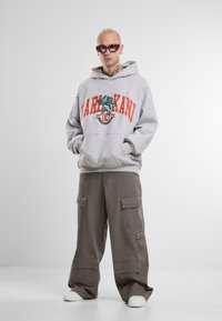 Gray hoodie with red and teal graphic text, paired with loose gray cargo pants featuring multiple pockets and white sneakers.