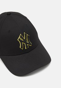 Schwarze Baseballmütze mit einem auffälligen gelben, gestickten "NY"-Logo. Das Design umfasst einen gebogenen Schirm und eine Sechsteilermusterung.