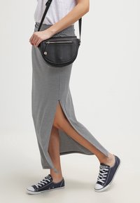 Jupe maxi rayée grise avec fentes latérales, associée à un sac bandoulière noir avec une poche zippée et des baskets en toile navy.