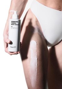 Flacone cilindrico bianco di "Crema Corpo Idratante e Rassodante" tenuto in una mano, crema applicata su una coscia, texture liscia, design minimalista.