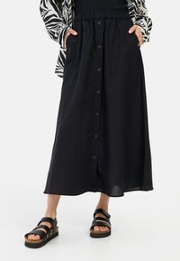 Zwarte linnen midi rok met een knopenlijst aan de voorkant, elastische tailleband en zijzakken. Gecombineerd met zwarte sandalen met brede banden en een kurken zool.
