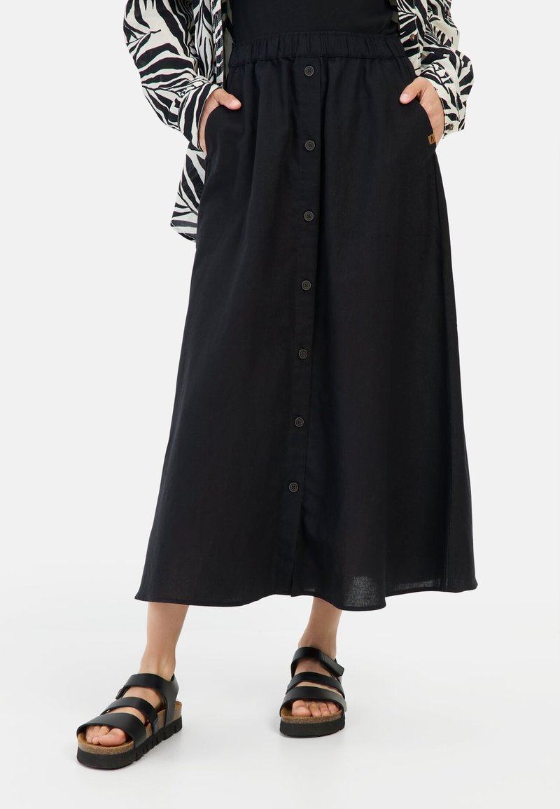 Zwarte linnen midi rok met een knopenlijst aan de voorkant, elastische tailleband en zijzakken. Gecombineerd met zwarte sandalen met brede banden en een kurken zool.