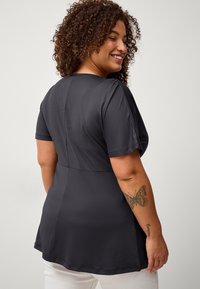 Haut noir à manches courtes avec une coupe décontractée, texture lisse et légère évasement à l'ourlet. Doté d'un col rond et de détails de couture au dos.