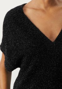 Haut court noir et duveteux à manches courtes avec un décolleté en V profond. Texture douce, coupe décontractée et fibres scintillantes pour un intérêt visuel.