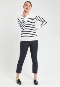 Pull-over rayé en blanc et bleu marine, avec un col rond, des accents de boutons sur l'épaule et un design en maille texturée. Associé à un pantalon texturé sombre et des mocassins brillants.