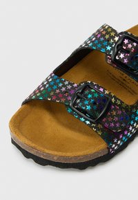 Sandaľ s otvorenou špičkou a dvoma čiernymi prackami pokrytými mnohobanými kovovými vzormi hviezd a mäkkou hnedou stielkou.