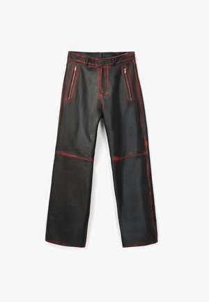 Pantalon en cuir synthétique noir avec des détails rouges usés, poches zippées à l'avant, passants pour ceinture et jambes larges.