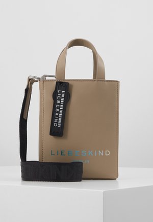 Mała beżowa, pionowa torba typu tote z dwoma uchwytami, czarnym odpinanym paskiem na ramię oraz czarną metką z napisem "LIEBESKIND" z przodu.