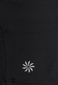 Pantalones cortos deportivos negros hechos de una tela suave, con un logo de explosión blanca en la parte inferior izquierda y detalles de costura sutiles.