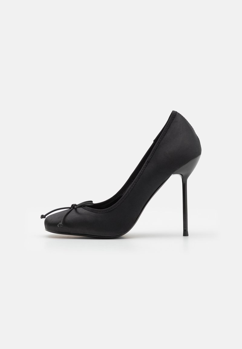 Escarpin noir à talons hauts avec une finition satinée, embout pointu et un petit nœud à l'avant. Il présente un talon stiletto fin.