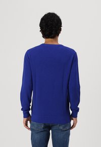 Pull en tricot bleu à manches longues et col rond, présentant une finition texturée et des poignets côtelés, vu de dos.