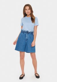 Světle modré tričko s krátkými rukávy, doplněné volnými modrými džíny s opaskem v pase. Černé plátěné boty na slip dokončují celý outfit.