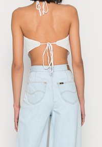 Bílá pletená halter top s designem na zavazování vzadu, v kombinaci se světle modrými džíny s vysokým pasem, které mají zadní kapsy a koženou visačku.