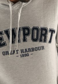 Grå hoodie med snörning, med kraftig marinblå text "NEWPORT GREAT HARBOUR 1990" över framsidan. Slät textur och avslappnad design.
