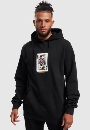 Man wearing black hoodie with a King of Spades playing card design and text "I got loyalty, got royalty inside my DNA" on front.
