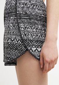 Pantalones cortos de estampado en blanco y negro con diseños geométricos. Terminados con un borde de pompones a lo largo del dobladillo y con un estilo de envoltura en el muslo.