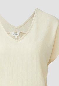 Haut en tissu texturé couleur crème avec manches courtes et décolleté en V avec un petit détail œillet dans le dos.
