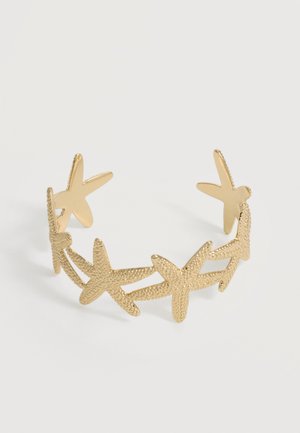 Bracelet manchette ouvert en or avec des étoiles de mer texturées liées en une chaîne continue sur fond blanc.