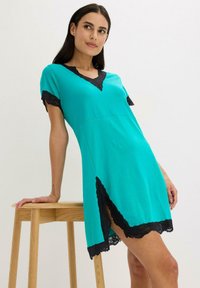 Abito turchese con maniche corte, bordo in pizzo nero attorno al colletto e all'orlo, con una fessura laterale. Tessuto morbido, design aderente.