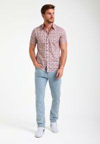 Korte mouwen shirt met roze en geometrische patronen, knoopsluiting aan de voorkant, gecombineerd met lichtblauwe spijkerbroek en witte sneakers.