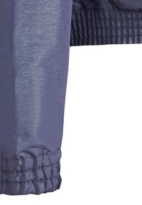 Lila elastisk manschett på en lätt, glänsande jacka med texturerad yta och rynkdetalj, som visar upp en slät tygkvalitet och sömlös design.