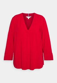 Red V-neck blouse with long sleeves, made of smooth fabric. Features a loose fit, side slits, and a straight hem. Tag visible at the neckline.