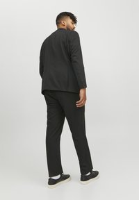 Traje negro con corte ajustado, con una apertura sencilla en la parte trasera, combinado con zapatillas negras y calcetines blancos. Textura de tela suave.