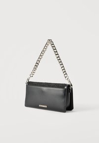 Μαύρη ορθογώνια τσάντα χειρός με αλυσίδα ασημένιου χρώματος ως λουρί και υφή στην επάνω πτερύγιο, με μικρό μεταλλικό λογότυπο "Steve Madden" στο μπροστινό μέρος.