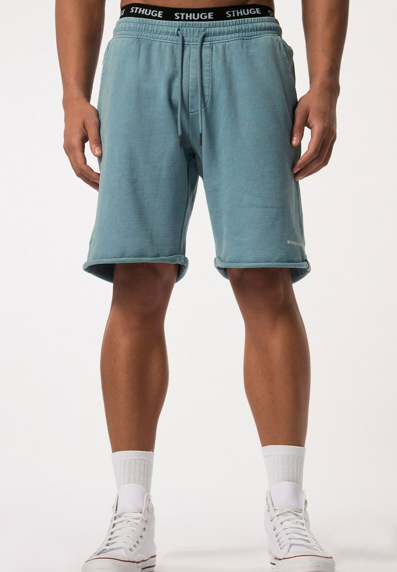 Lichtblauwe katoenen shorts met een elastische tailleband, voorzien van zwarte trekkoorden en een logo. Opgerolde zoom en zijzakken.