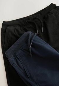 Zwei Paar Jogginghosen; eine schwarz und eine marineblau. Beide verfügen über elastische Taillenbünde mit verstellbaren Kordeln und gerippten Bündchen.