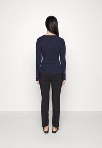 Haut à manches longues côtelé de couleur marine associé à un pantalon noir ajusté. Les deux vêtements ont une texture lisse et une coupe près du corps.