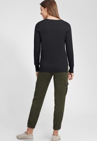 Top nero a maniche lunghe con scollo a barca, abbinato a pantaloni cargo oliva con tasche laterali e polsini elasticizzati. Scarpe lacci grigio chiaro.