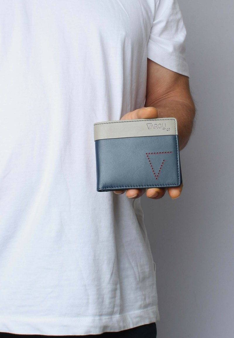 Blue leather wallet with a grey top edge, featuring a triangular cutout and red stitching detail, held in a hand against a plain background.
