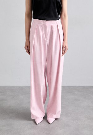 Pantalons taille haute rose clair avec plis et coupe décontractée, fabriqués dans un tissu texturé, associés à des escarpins roses pointus.