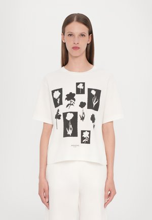 Weißes T-Shirt mit kurzen Ärmeln, das mit schwarzen Blumenmustern in verschiedenen Formen und Größen verziert ist. Aus weichem Baumwollstoff mit lockerer Passform.
