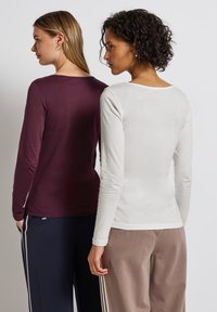 Langsleeve T-shirts in bordeaux en witte jersey stof. Eenvoudige, ronde halslijnen met een getailleerd ontwerp. Achteraanzicht, gedragen met broek.