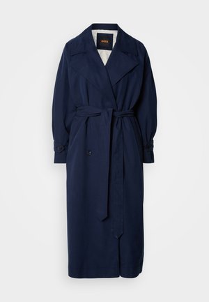 Trench-coat bleu marine avec une taille ceinturée, un grand col et des poignets boutonnés. Fabriqué à partir d'un tissu lisse, il possède une doublure matelassée.