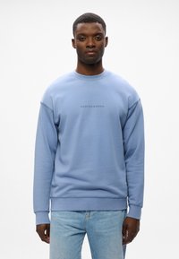 Sudadera azul claro con cuello redondo y puños acanalados. Presenta el logo "SCOTCH & SODA" en el centro. Fabricada con una mezcla de algodón.