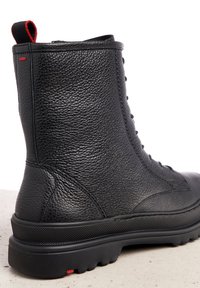 Bottine en cuir noir avec une finition texturée, bout rond, col rembourré, tirette rouge et semelle en caoutchouc robuste avec adhérence.